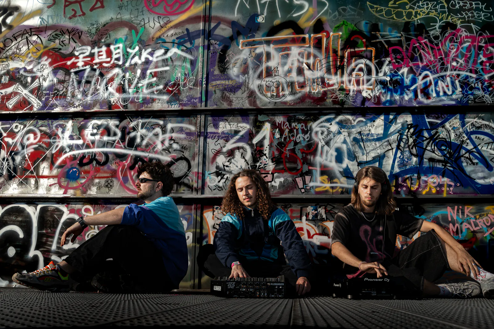 Trio de musiciens assis avec leurs instruments devant un mur couvert de graffitis
